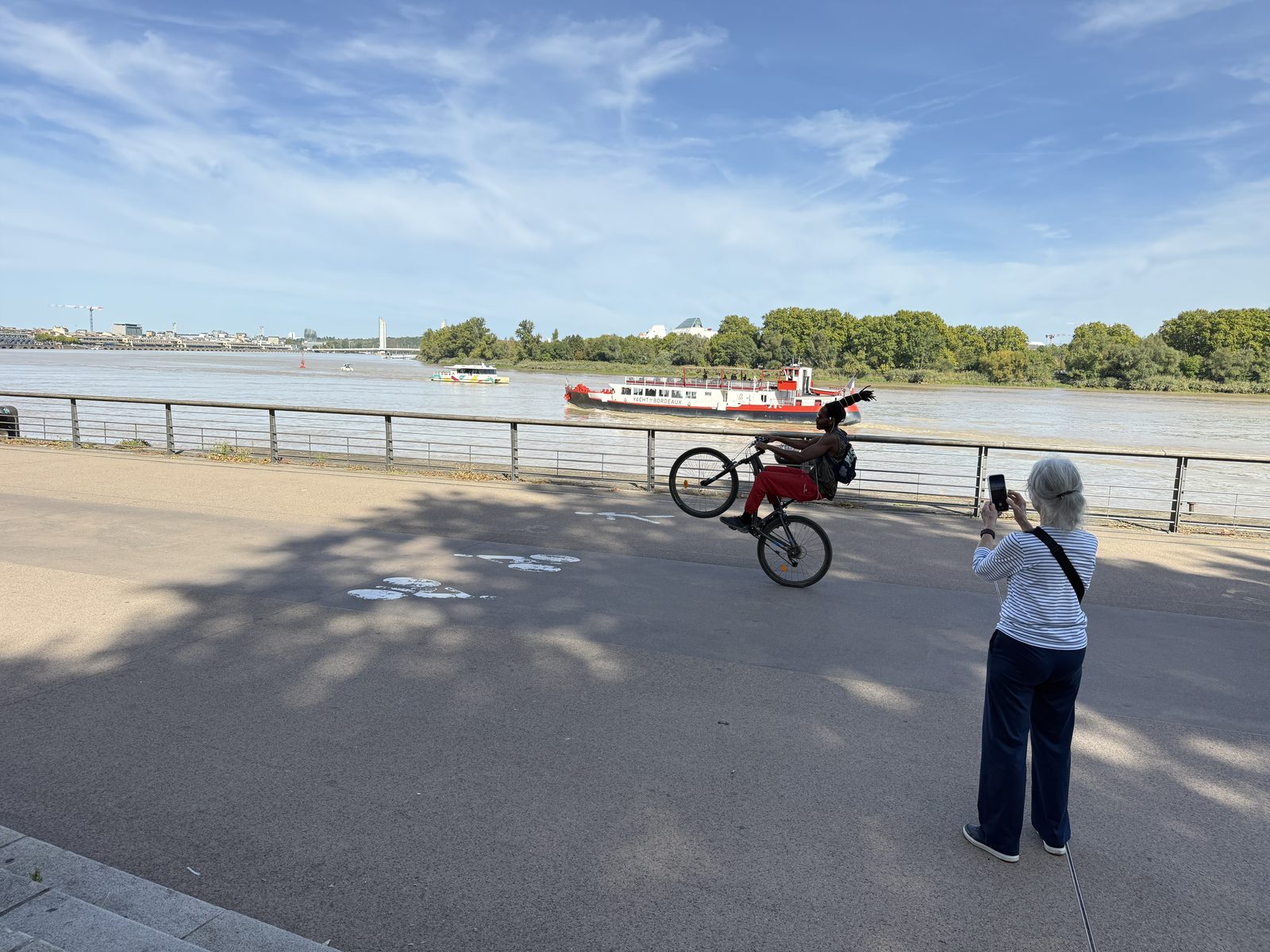 Liz photographing a street performer popping a wheelie along the riverside promenade.
