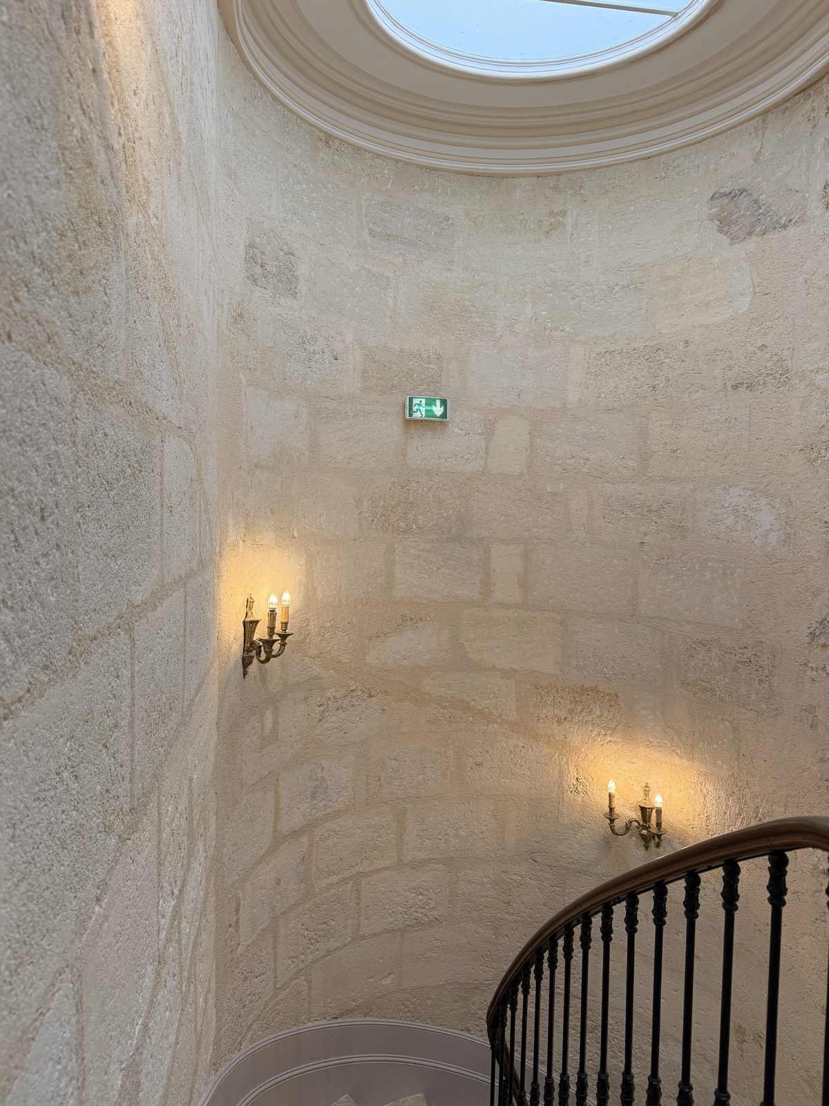The villa's beautiful stone spiral stairwell, lit from an oculus skylight overhead — architectural detail worth stopping to photograph.